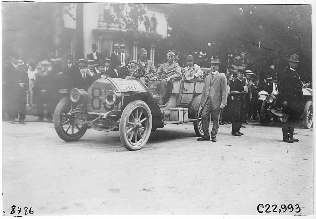 Press car #83 on city street with crowd of men in background, at 1909 Glidden Tour