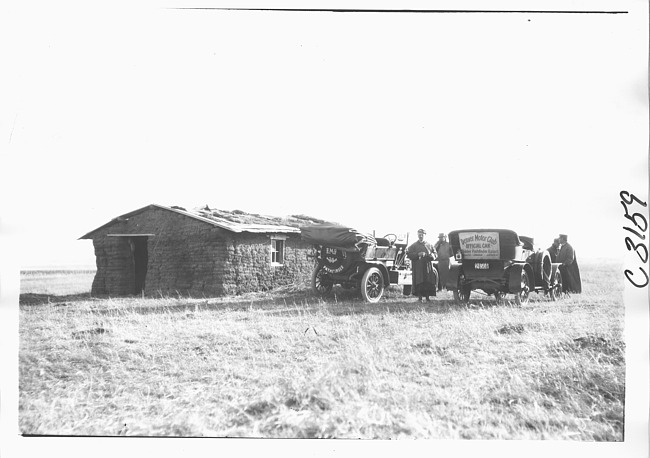 E.M.F. car and Denver Motor Club escort car parked next to sod house, on pathfinder tour for 1909 Glidden Tour