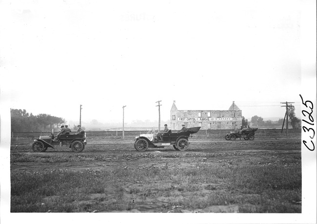 Three cars pass First Capitol of Kansas building, on pathfinder tour for 1909 Glidden Tour