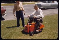 Demonstrating a Mow-Cycle riding rotary lawn mower, 1955